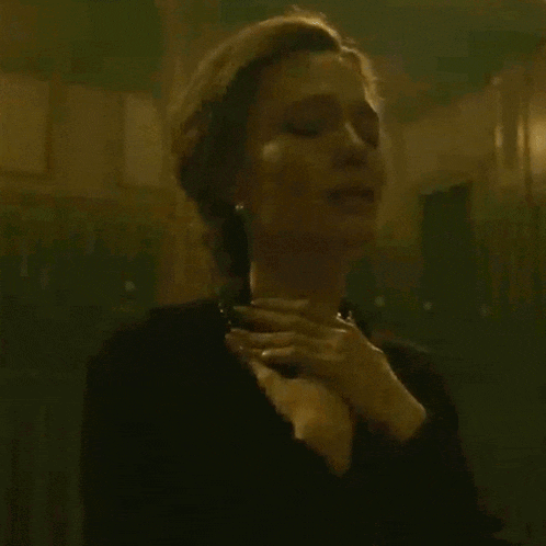 a woman in a black dress is holding her chest with her hand .