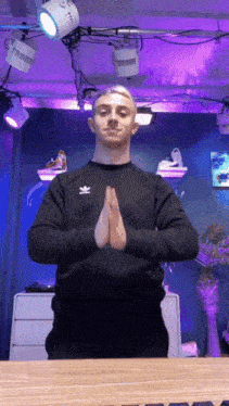 a man wearing a black adidas sweatshirt is praying with his hands folded