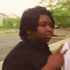 a man with dreadlocks is standing in a parking lot with a white shirt on .