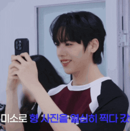 a young man is taking a picture of himself with a cell phone in front of a sign that says " 미소로 "