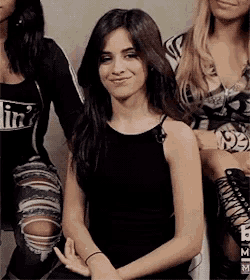 a woman in a black tank top and ripped jeans is sitting next to another woman .