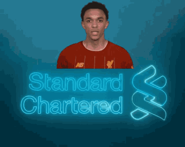 a man in a red shirt is standing in front of a blue sign that says standard chartered
