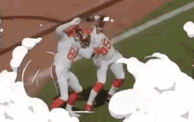 two football players are fighting on a field with smoke coming out of them .