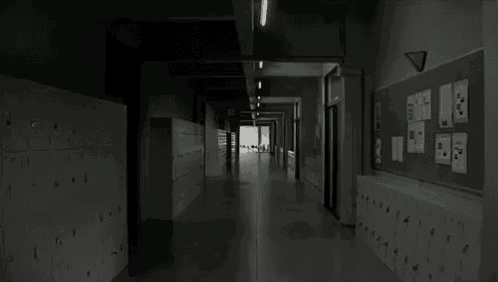 a black and white photo of a hallway in a school with lockers .
