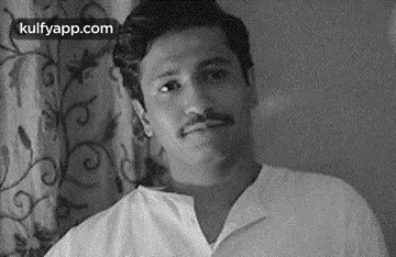 a man with a mustache is sitting in front of a curtain in a black and white photo .