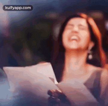 a woman is laughing while holding a piece of paper in her hands .