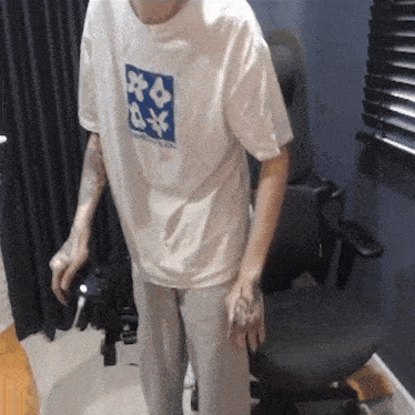a man wearing a white t-shirt with flowers on it is standing next to a chair