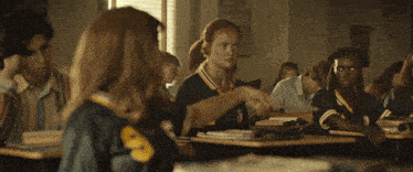 a girl with the number 8 on her shirt is sitting at a desk in a classroom