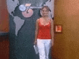 a woman in a red tank top and white pants is standing in front of a wall with a map on it .