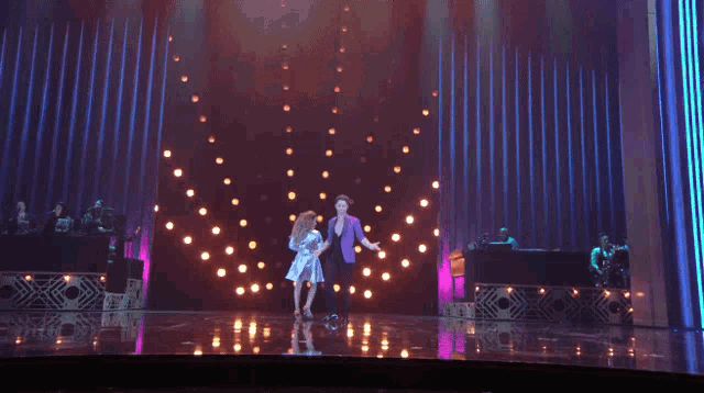 a woman in a purple dress is dancing on a stage with a man in a purple suit