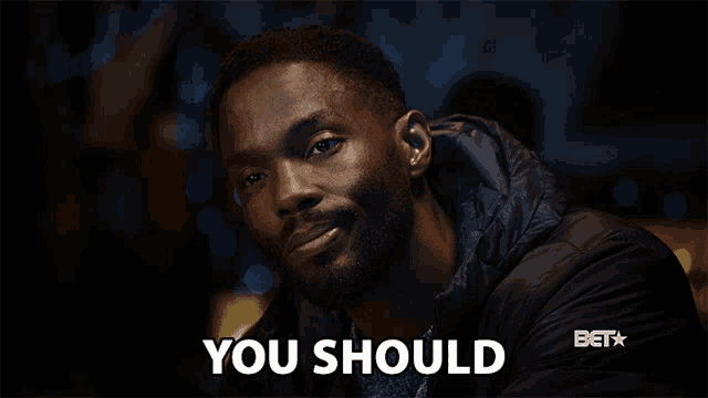 a man in a black jacket is smiling and says " you should "