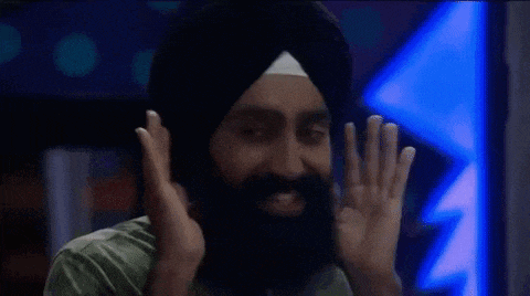 a man with a beard wearing a turban is holding a glass of whiskey in front of his face .