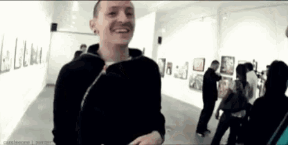 a man in a black jacket is smiling in a museum while a group of people are standing around him .