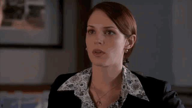a woman with red hair is wearing a black jacket and a floral collared shirt