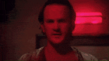 a man with a beard is standing in a dark room with a red light behind him .