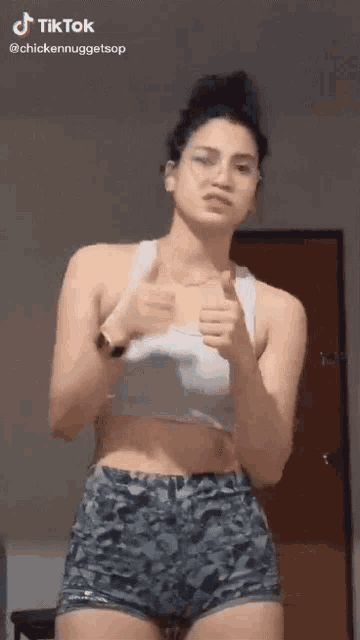 a woman wearing shorts and a tank top is giving a thumbs up sign .