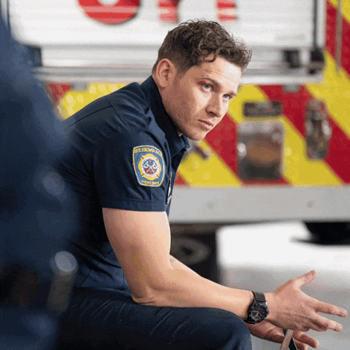 a man sitting in front of an ambulance has a patch on his shoulder that says emergency services