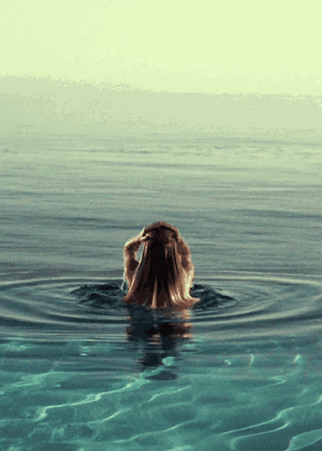a woman is swimming in the ocean with her head in her hands