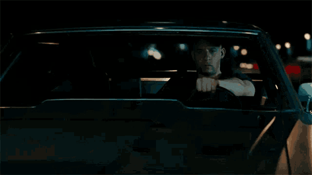 a man in a black shirt is driving a car