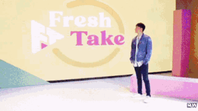 a man in a denim jacket stands in front of a fresh take sign