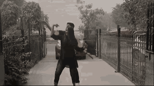 a man and a woman are dancing in a driveway in front of a fence .