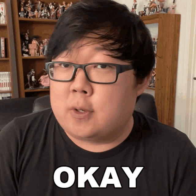 a man wearing glasses and a black shirt with the word okay on it