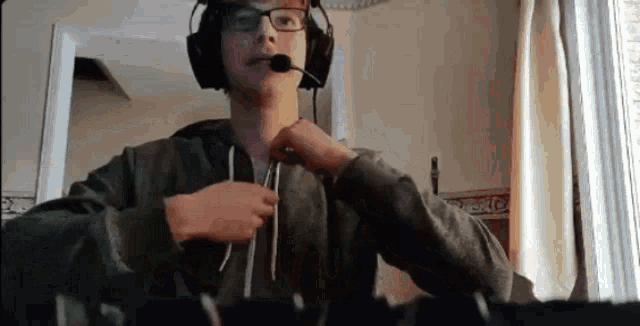 a young man wearing headphones and glasses is sitting in front of a computer .