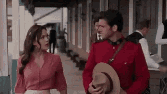 a man in a red uniform and a woman in a pink shirt are standing next to each other on a sidewalk .