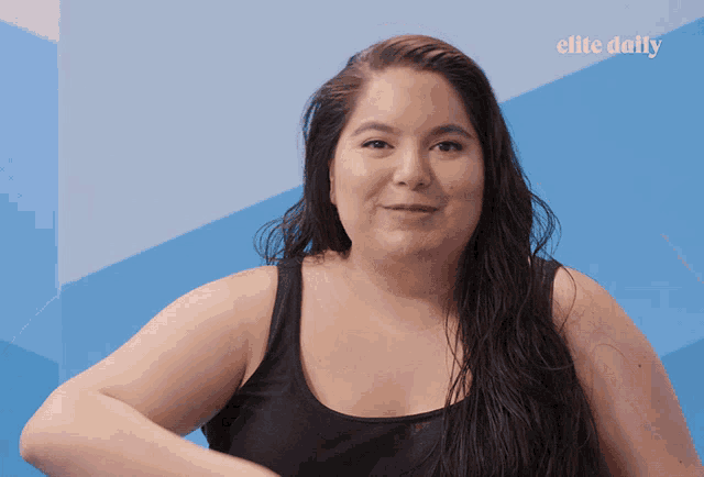 a woman in a black tank top stands in front of a blue wall with elite daily written on it