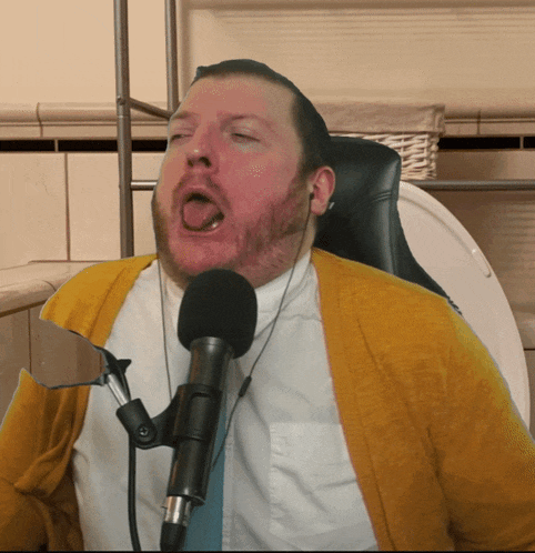 a man in a yellow sweater is singing into a microphone while sitting on a toilet