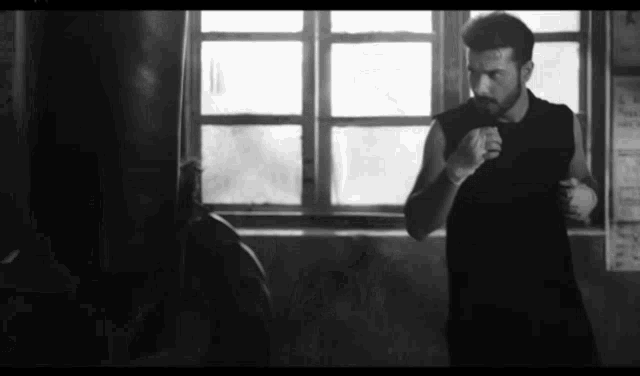a black and white photo of a man in a boxing ring with a punching bag .