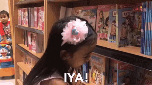 a little girl with a flower in her hair is looking at books and says iya