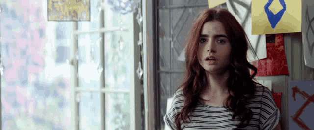 a woman in a striped shirt stands in front of a window with a blue diamond on it