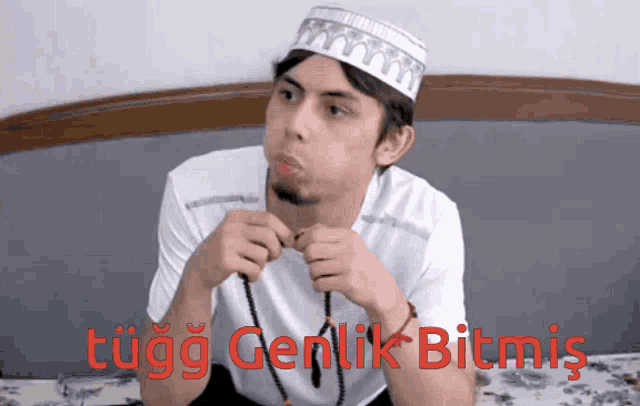 a man wearing a white hat is sitting on a bed with the words tugg genlik bitmis written in red