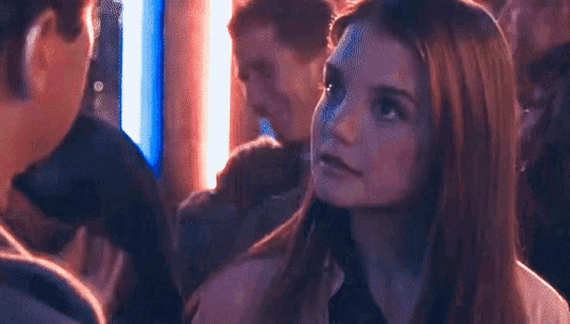 a woman is looking up at a man in a crowd of people in a dark room .