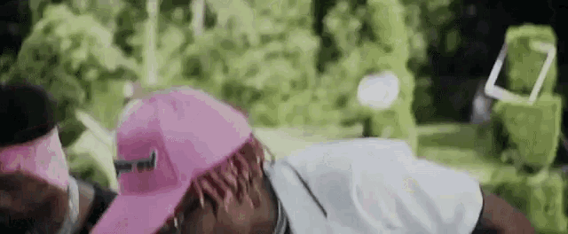 a man wearing a pink hat and sunglasses is laying down in a park .