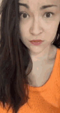 a close up of a woman 's face with an orange shirt on