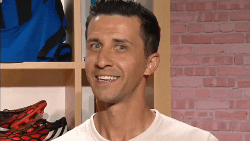 a man in a white shirt is smiling in front of a pink brick wall