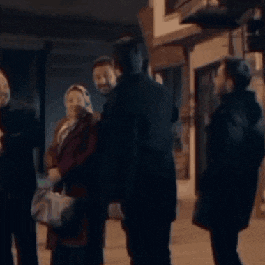 a group of people are standing on a sidewalk talking to each other at night .
