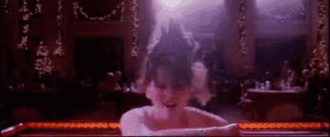 a woman is dancing in a dark room with a purple light behind her .