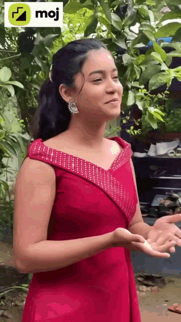 a woman in a red dress is standing in front of a tree and holding something in her hands .