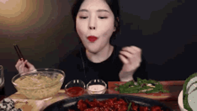 a woman is sitting at a table eating food with chopsticks and a bowl of noodles .