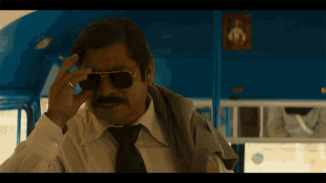 a man with a mustache wearing sunglasses and a cigarette in his hand