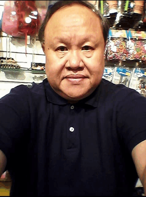 a man in a black polo shirt takes a selfie in front of a wall of toys