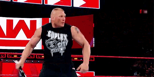 a wrestler in a black tank top is standing in a wrestling ring .