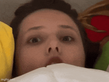 a close up of a woman 's face with a surprised look on her face while laying in bed .