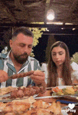 a man and a woman are sitting at a table eating food with a heart in the corner
