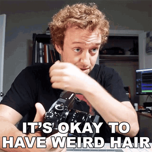 a man holding a camera with the words it 's okay to have weird hair below him
