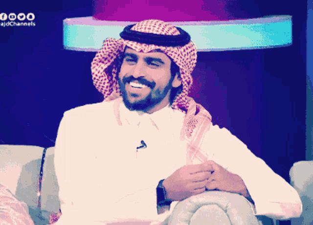 a man wearing a turban and a white shirt is smiling in front of a sign that says ajdchannels
