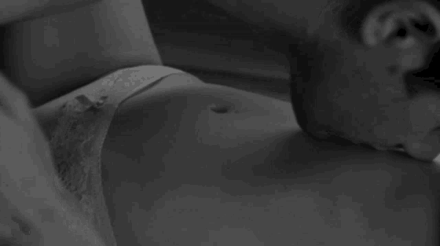 a black and white photo of a man kissing a woman 's stomach .
